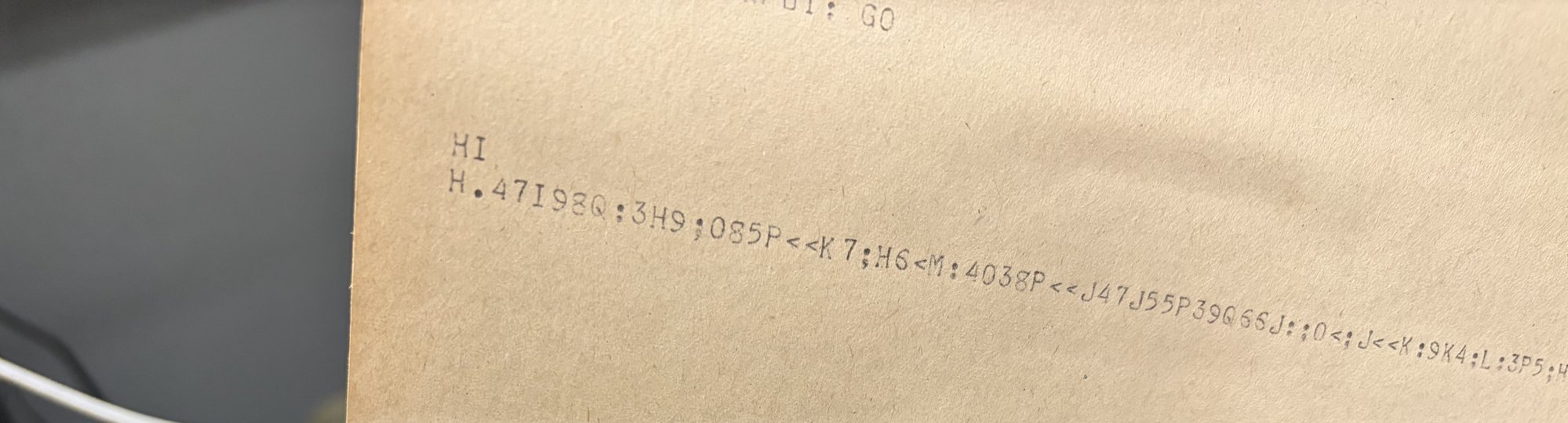 Teletype paper showing a line of random ASCII characters instead of the digits of pi.
