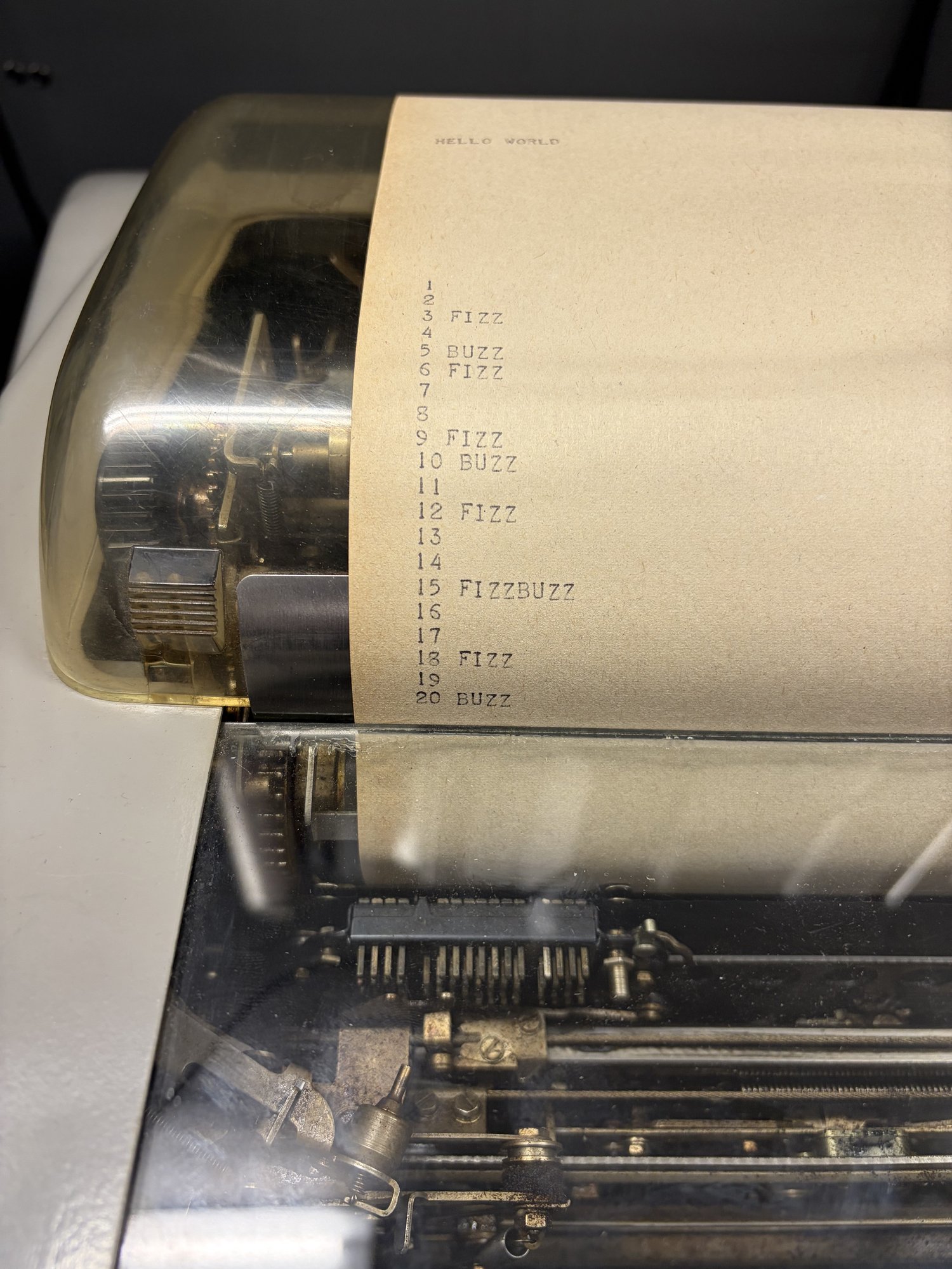 Teletype paper showing HELLO WORLD followed by fizzbuzz output.