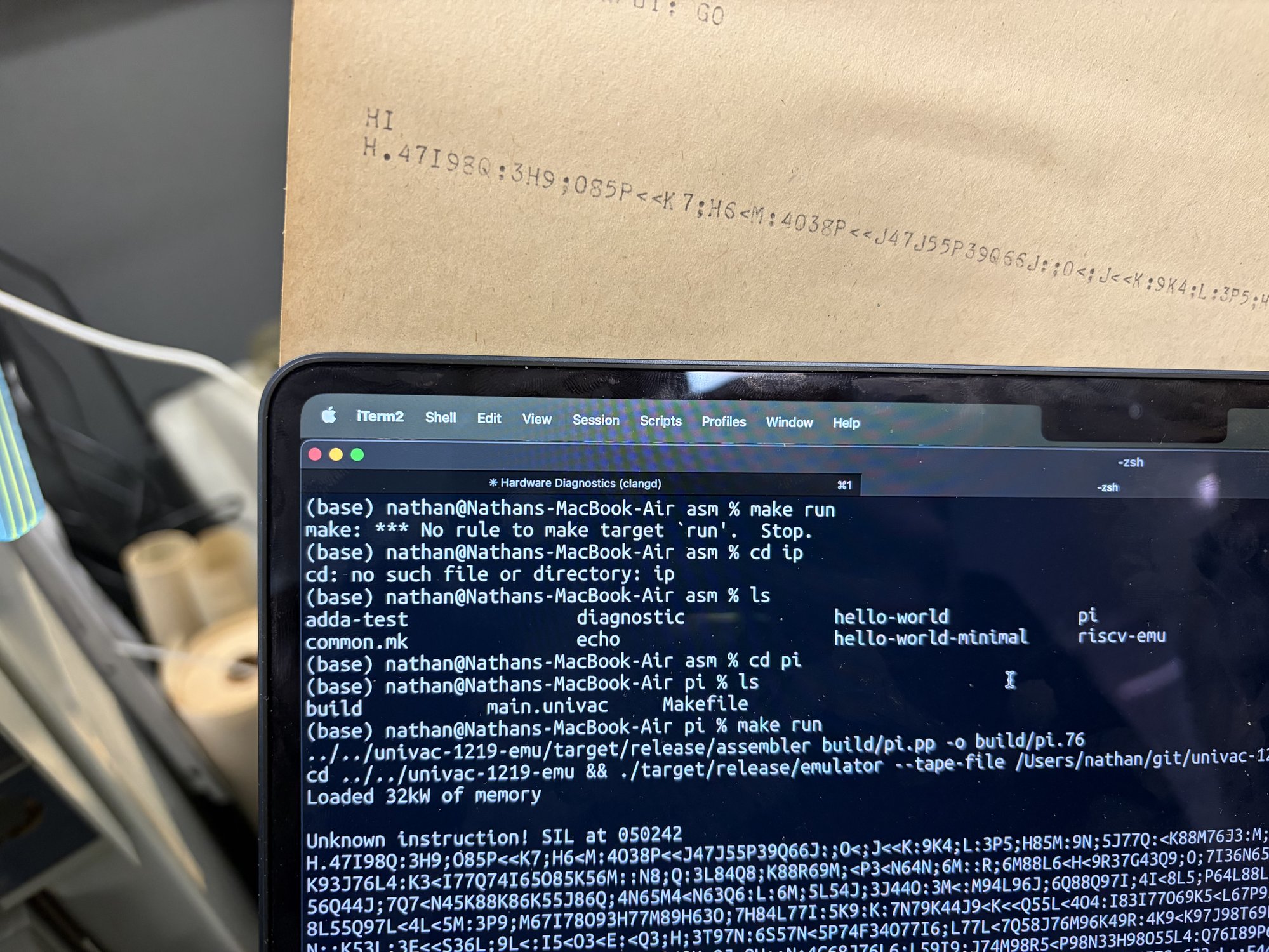 Teletype paper above a laptop terminal, both showing the same garbage output from the pi program.