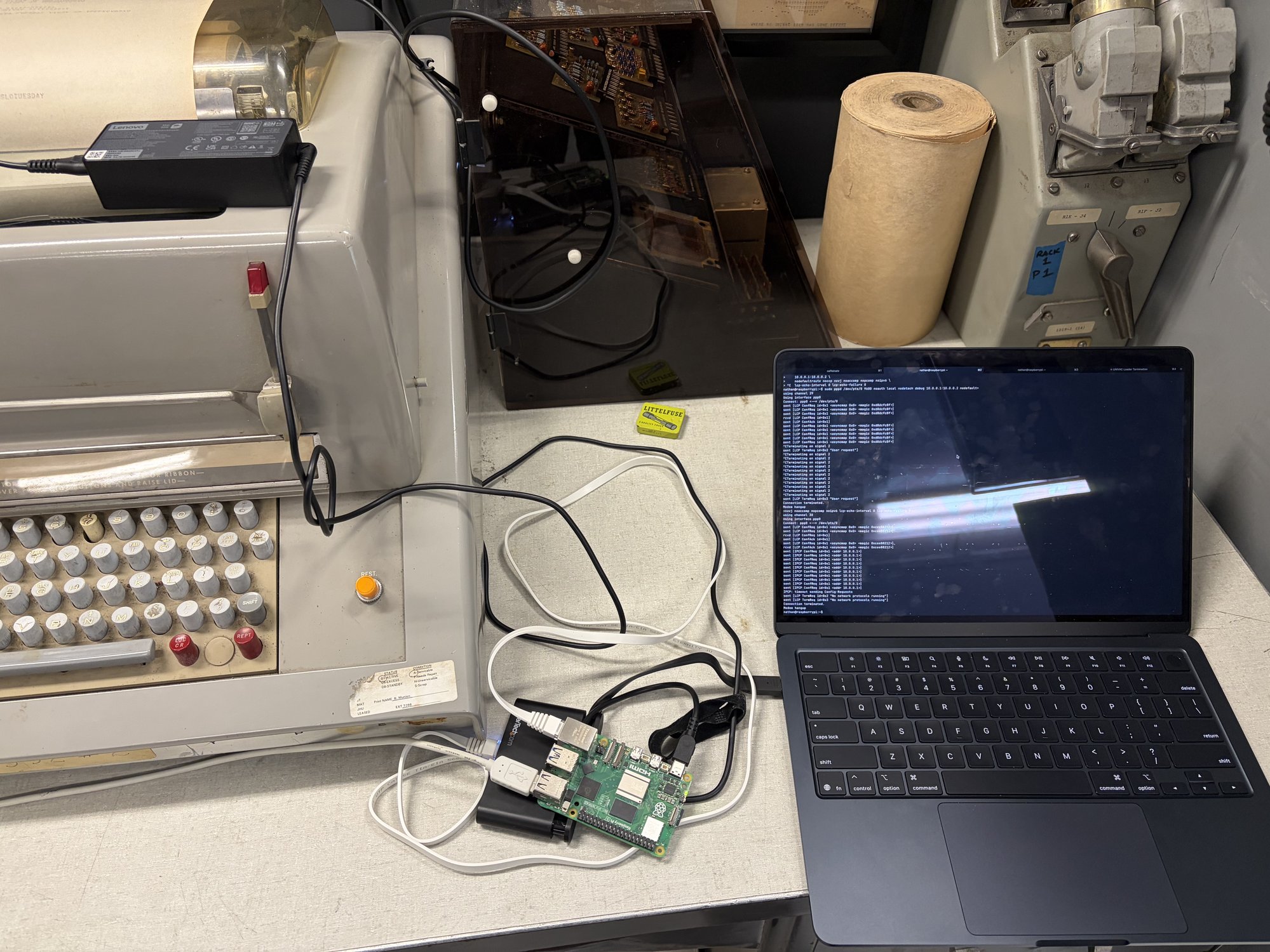 A workbench with the UNIVAC teletype on the left, a Raspberry Pi in the middle, and a Mac laptop on the right.